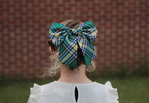Girl wearing large Green, yellow plaid hair bow.  Looking towards brick wall.