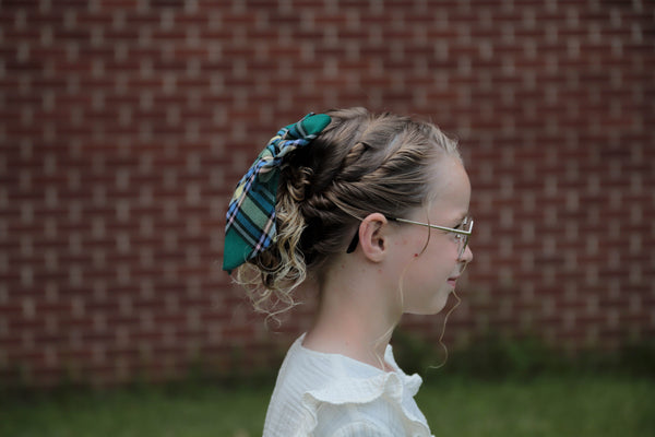 side view of girl with glasses and blond hair wearing Alberta tartan hair bow