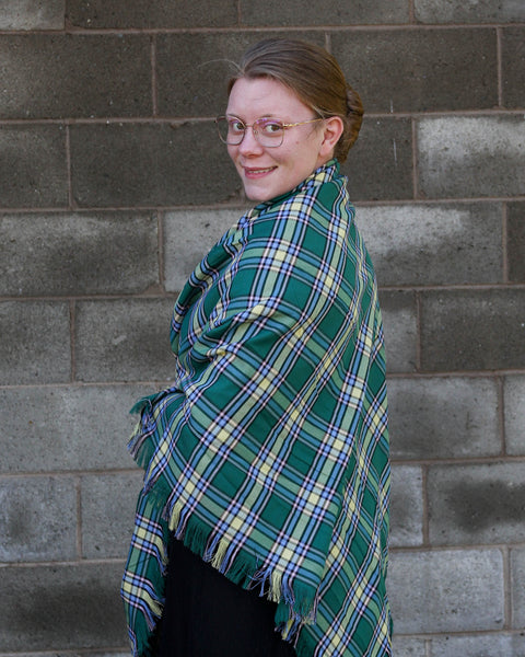 Person wearing a green plaid Alberta tartan shawl against a brick wall
