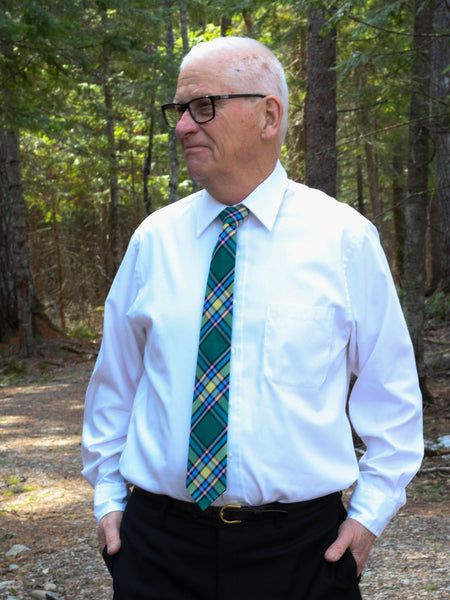Man wearing a white shirt and green plaid tie standing in a forest.