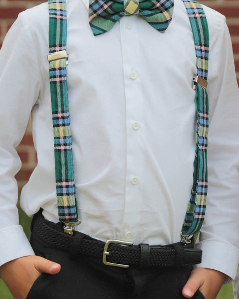Person wearing a white shirt with green plaid alberta tartan suspenders and bow tie against a blurred background