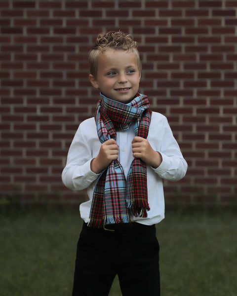 Young boy wearing a Anderson plaid scarf in front of a brick wall