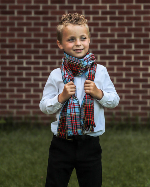 Young boy wearing a plaid scarf in front of a brick wall