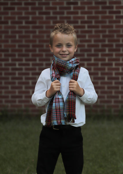 Young boy wearing a plaid scarf by Taylors Tartans in front of a brick wall
