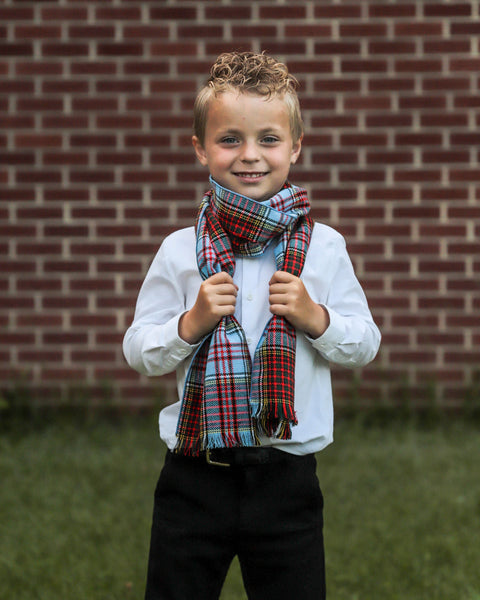 Young boy wearing a plaid scarf in front of a brick wall