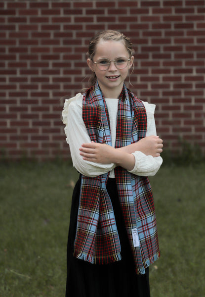 Young girl wearing Anderson tartan scarf over a white shirt with a brick wall background
