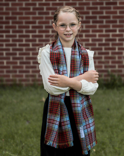 Young girl wearing an Anderon tartan  plaid scarf in front of a brick wall.