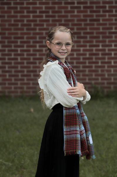 Girl wearing a blue and mauve scarf and white shirt against a brick wall.