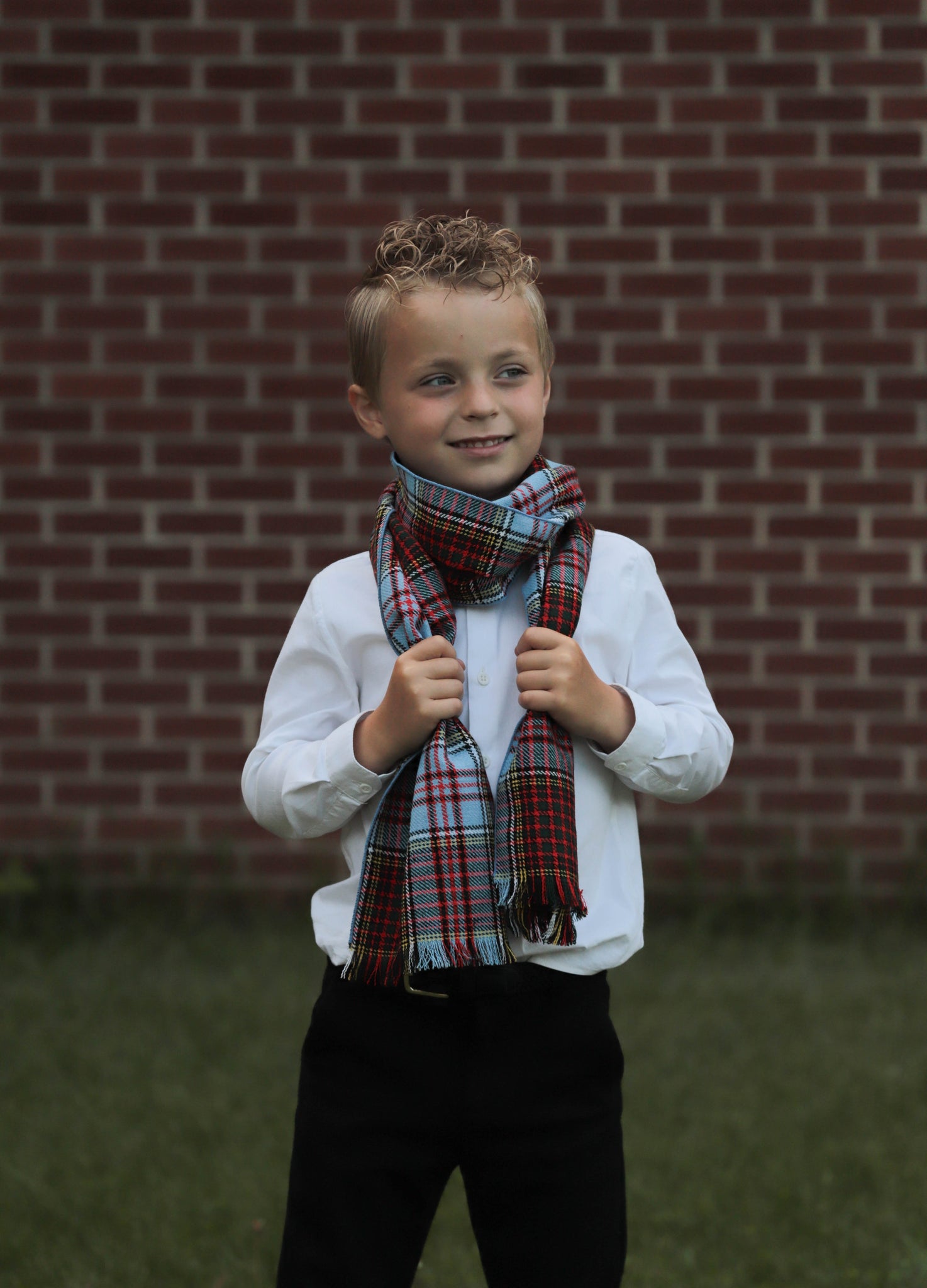 Young boy wearing an Anderson plaid scarf in front of a brick wall