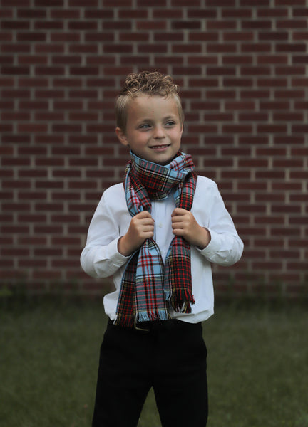 Young boy wearing an Anderson plaid scarf in front of a brick wall