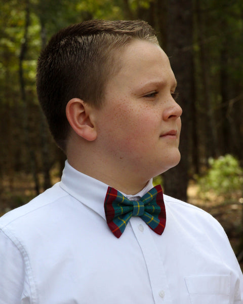 Young boy wearing a white shirt and red green white gold British Columbia tartan plaid bow tie outdoors
