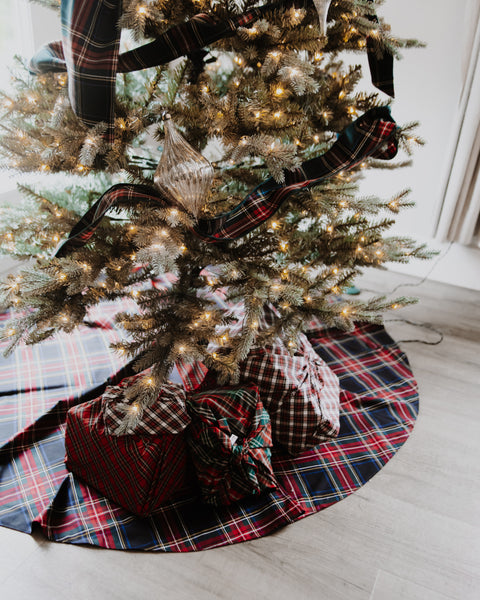 a black stewart tartan black red white and yellow plaid christmas tree skirt underneath a lit christmas tree with wrapped presents