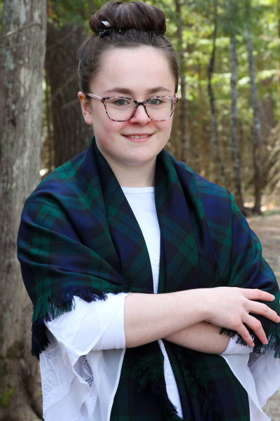 A young woman wearing a Black Watch tartan navy and green plaid blacket scarf.