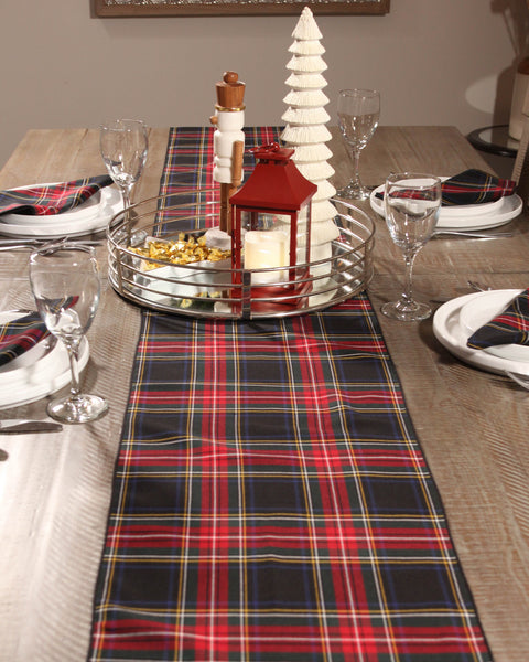 Dining table set with a black and red plaid runner, candles, and glasses.
