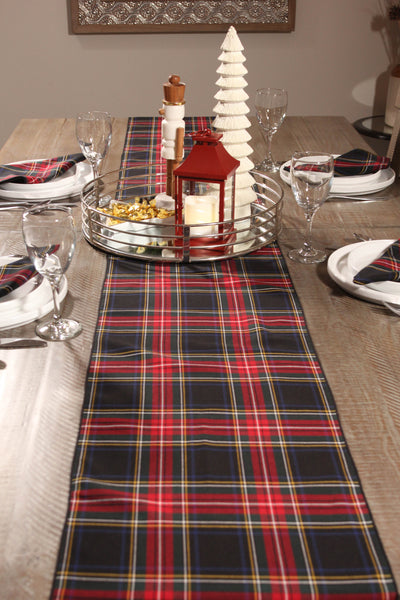 Black Stewart tartan table runner with matching napkins on a wooden table, accented with Christmas decorations.