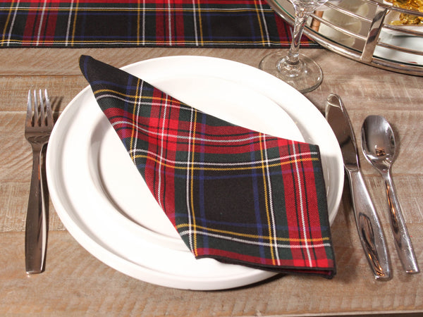Black Stewart Plaid napkin on a white plate with cutlery on a wooden table.
