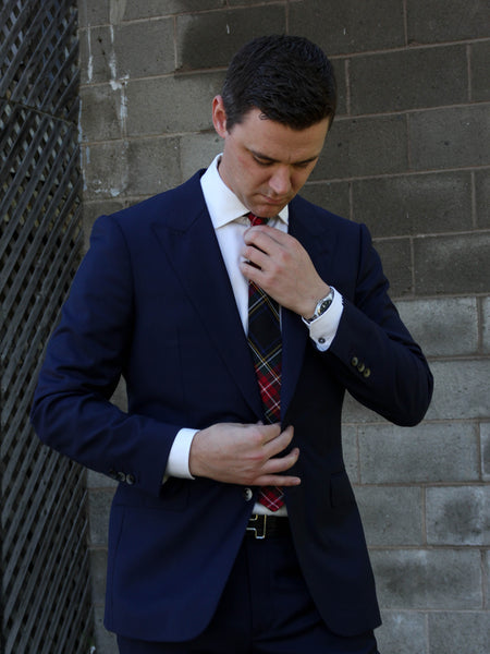 Man adjusting his Black Stewart tartan tie against a brick wall