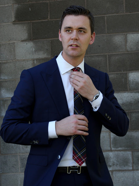 Man adjusting his plaid tie against a brick wall