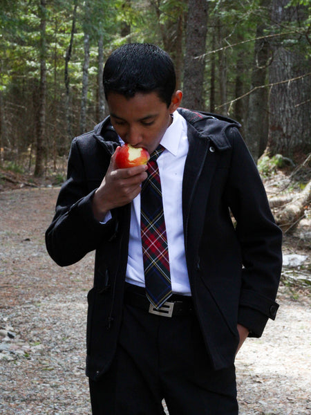 Person in formal attire eating an apple in a forest setting