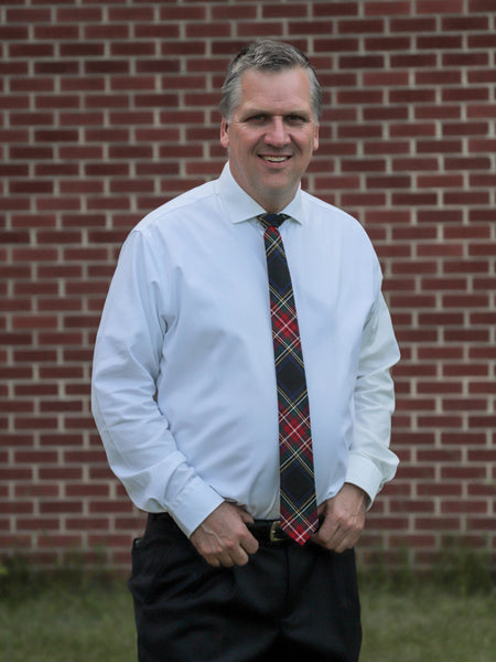 Man wearing a white shirt and plaid tie standing in front of a brick wall