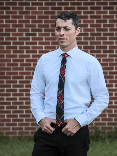 Man wearing a light blue dress shirt and plaid tie against a brick wall.