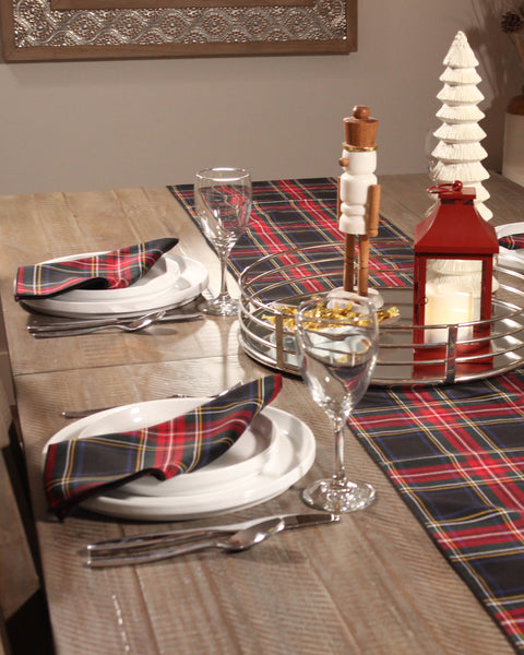 Dining table set with Black Stewart tartan  plaid table runner and napkins, and glassware on a wooden table.