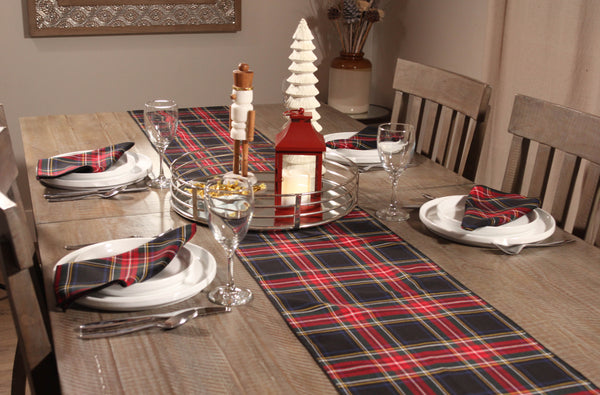 Black and red plaid table runner on a wooden table, with matching napkins on white plates, accented by festive Christmas decorations.