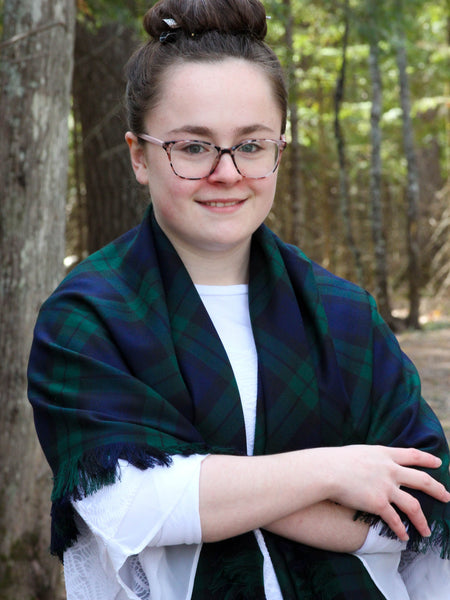 woman wearing a navy and green plaid shawl in a forest setting