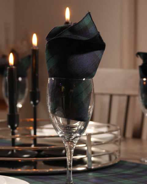 Decorative Black Watch tartan plaid napkin in a wine glass with candles and a chair in the background