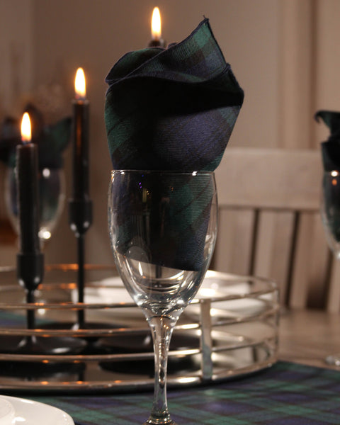 Decorative navy and green plaid napkin in a wine glass with candles in the background.