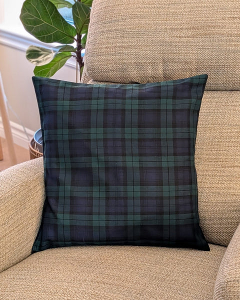 Navy and green plaid pillow on a beige couch with a plant in the background