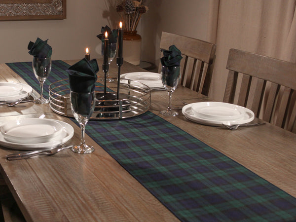 Dining table set with navy and green plaid runner, plates, glasses, and candles.