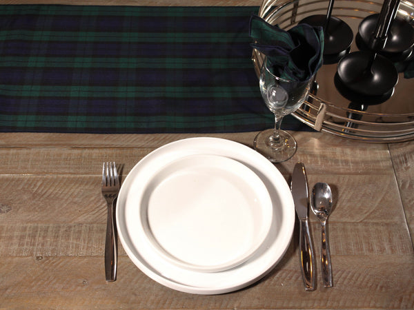 Dining table setting with white plates, silverware, and a plaid runner.