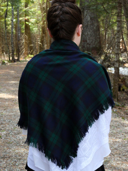 woman wearing a dark green and navy plaid shawl in a forest setting