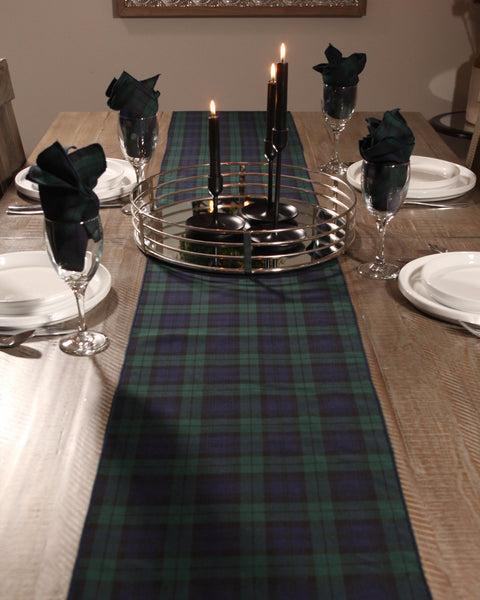 Dining table set with a black and green tartan runner, candles, and glassware.