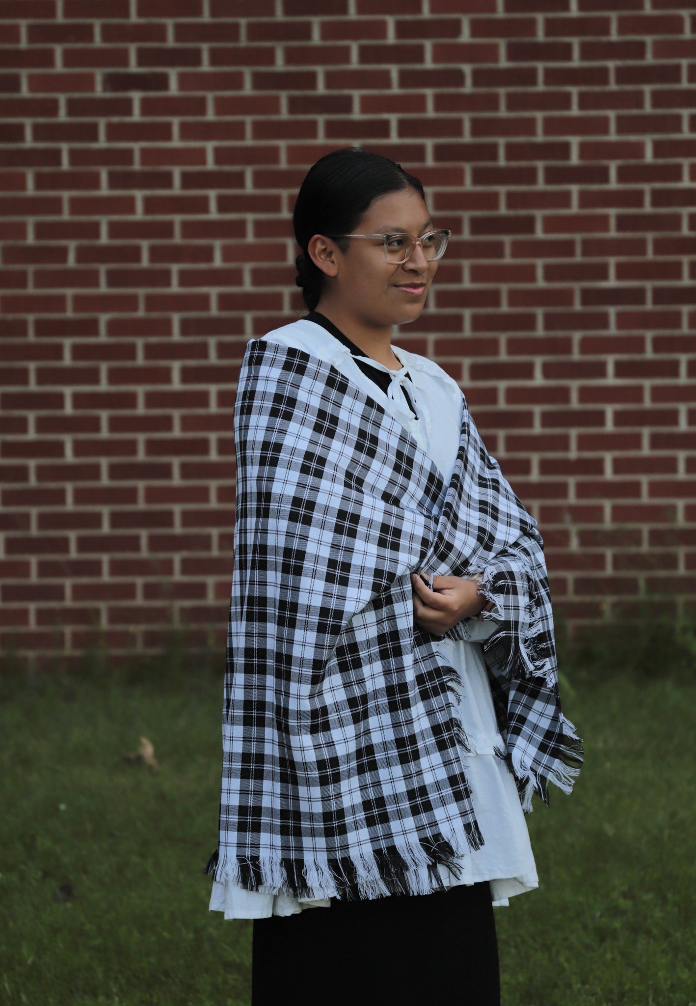 Person wearing a black and white checkered Ershine tartan shawl in front of a brick wall.