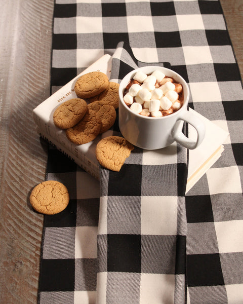 Cup of hot chocolate with marshmallows and cookies on a black and white checkered plaid tablecloth with matching napkins