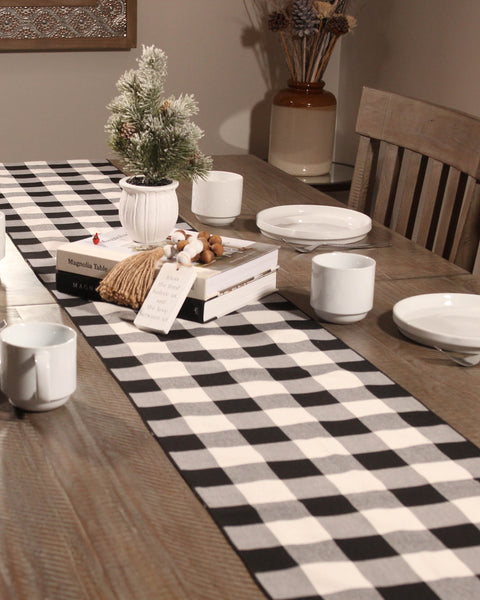 Dining table with a black and white checkered runner, decorative items, and a small Christmas tree.