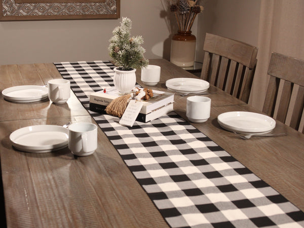 Dining table set with checkered table runner, plates, cups, and decorative items.