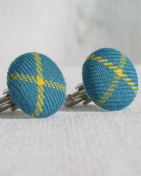 Pair of teal blue and yellow patterned cufflinks on a white background