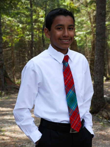 Young boy wearing a white shirt and red plaid tie outdoors with trees in the background