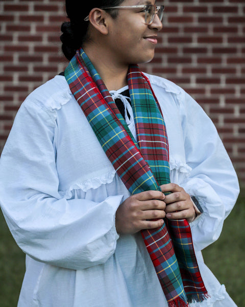 Person wearing a red and green plaid British Columbia scarf in front of a brick wall.