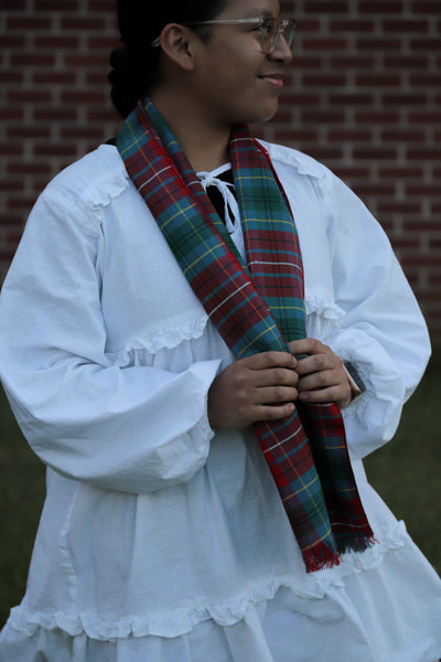 Person wearing a white blouse with a British Columbia tartan red, teal, and white plaid scarf in front of a brick wall
