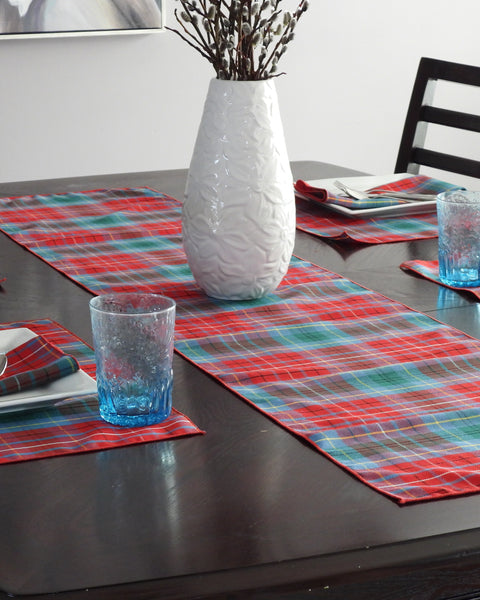 Dining table set with red and blue plaid British Columbia tartan table runner, placemats, glasses, and a white vase.