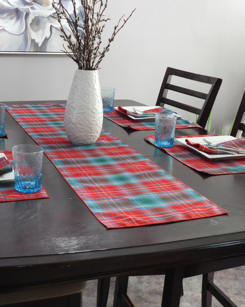 Dining table set with teal and red plaid placemats, glasses, and a vase.