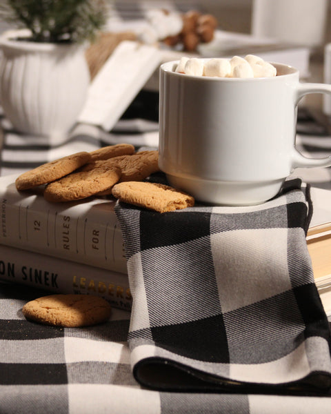 White mug with hot chocolate and marshmallows on a buffalo white and black tartan cloth with cookies nearby