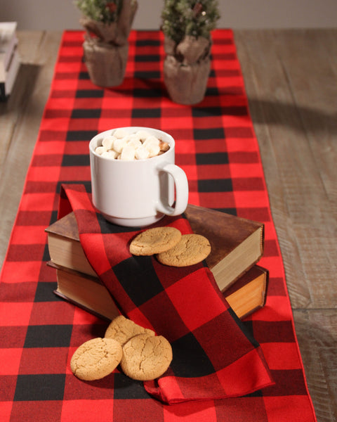 White mug with hot chocolate and marshmallows on a black and red buffalo check napkin on a stack of books with cookies, all on a red and black Buffalo check  table runner.