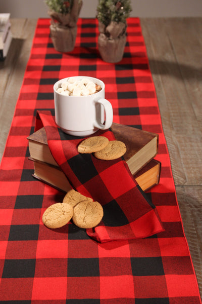 Buffalo check table runner with a matching napkin placed on a stack of books, accompanied by hot chocolate and cookies.