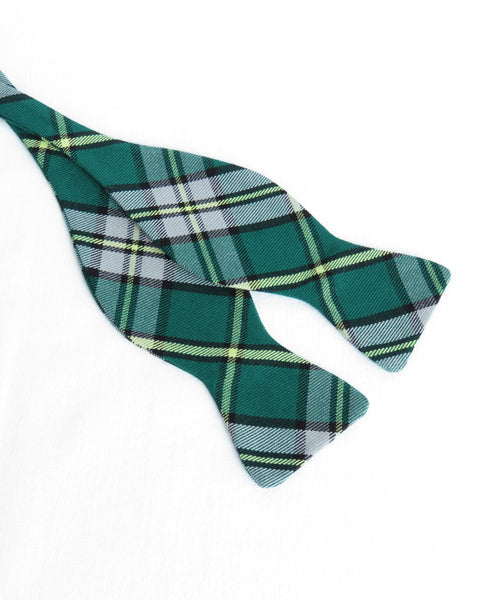 Green, yellow, gray, black plaid self tie bow tie laying open on a white table