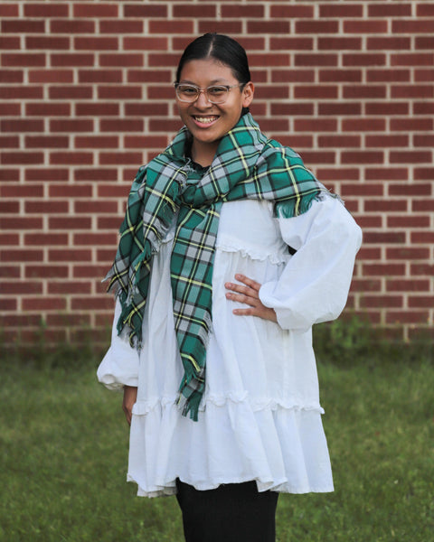 Person wearing a green plaid scarf in front of a brick wall